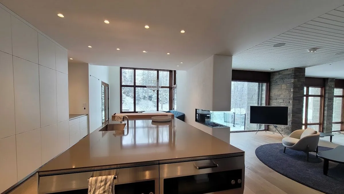 Open-plan kitchen and living room with a TV on a floor stand, recessed lighting and tall windows onto a snowy yard